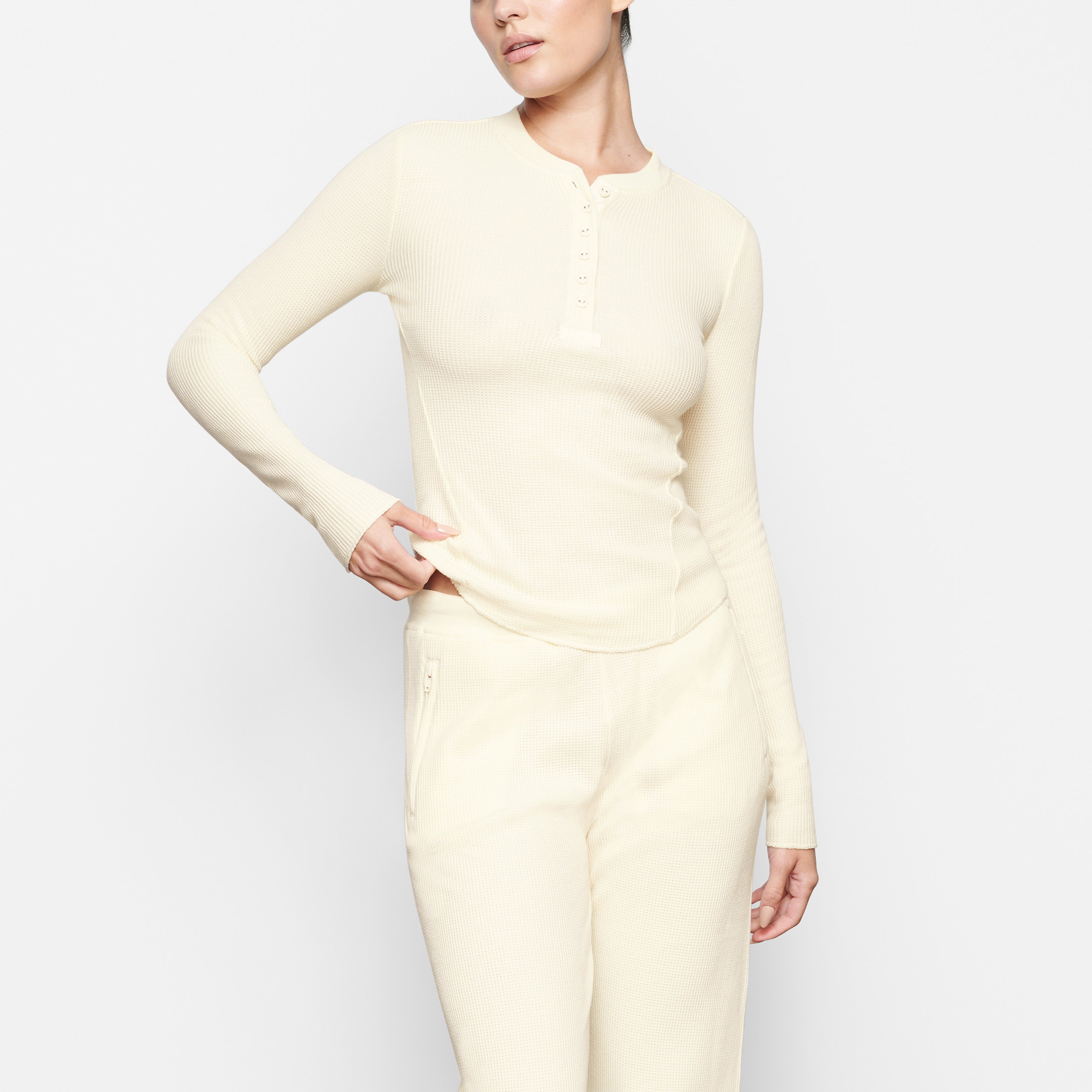 A MODEL STANDS FACING FORWARD WEARING THE SKIMS WAFFLE LONG SLEEVE HENLEY IN CREAM | SEE: XXS, XS, S