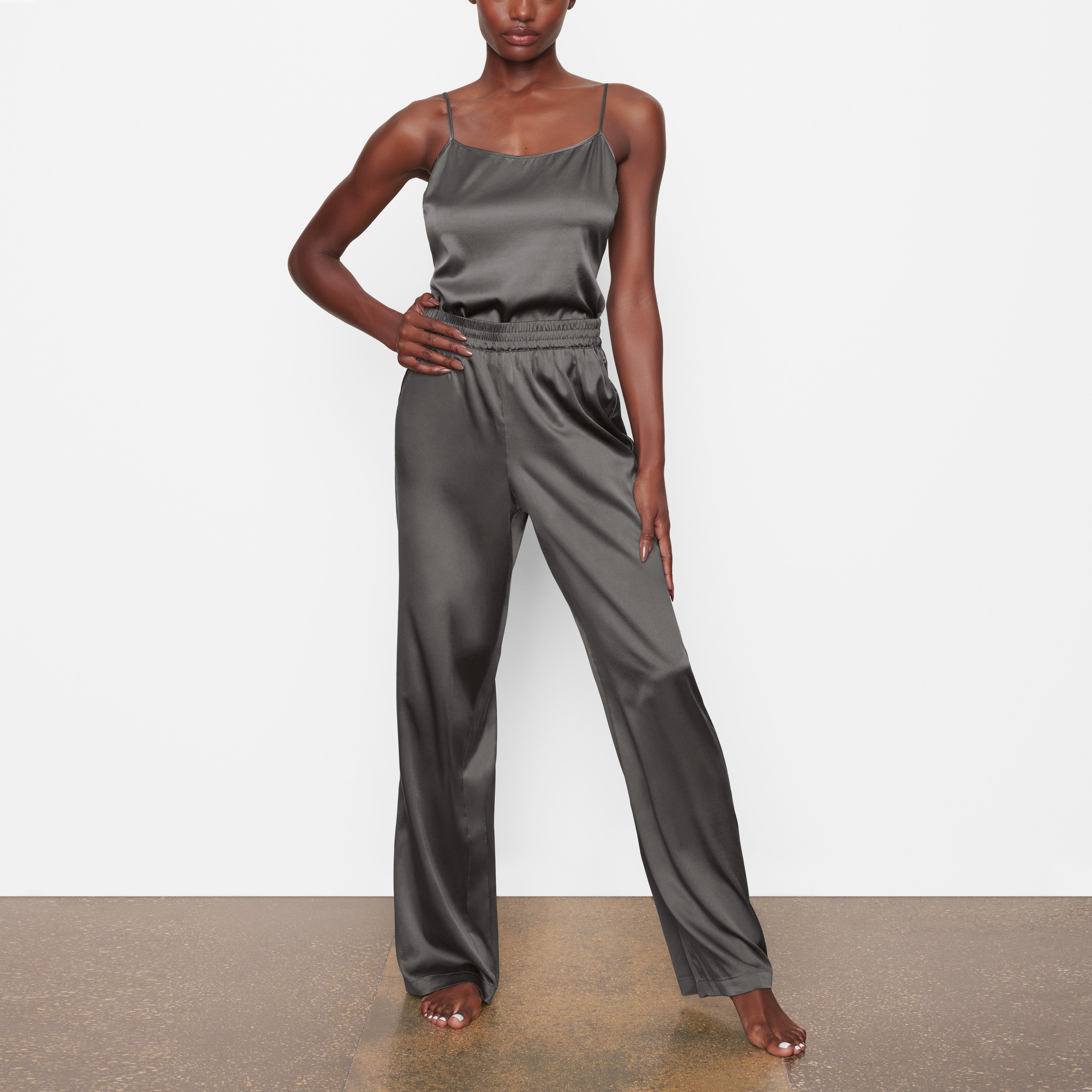 A MODEL STANDS FACING FORWARD WEARING THE SKIMS SILK WIDE LEG SLEEP PANT IN GUNMETAL | SEE: XXS, XS, S