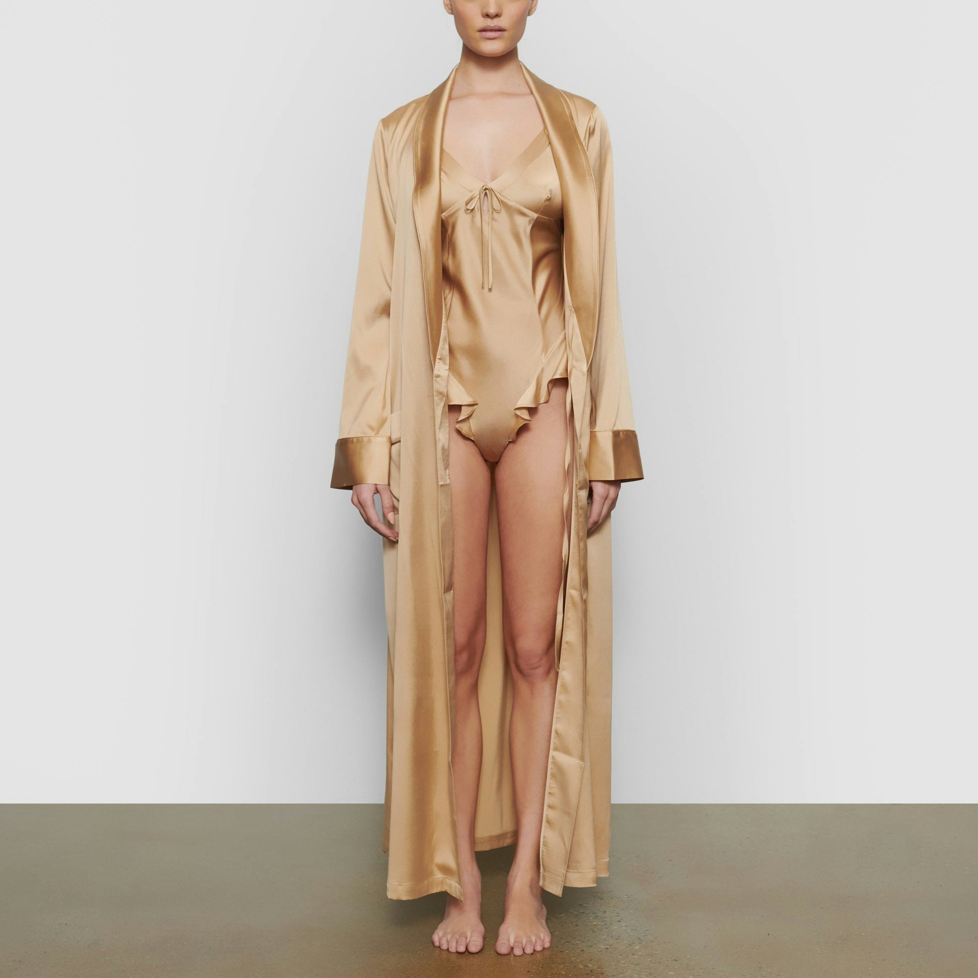 A MODEL STANDS FACING FORWARD WEARING THE SKIMS SILK SLEEP ROBE IN HONEY | SEE: XXS, XS, S