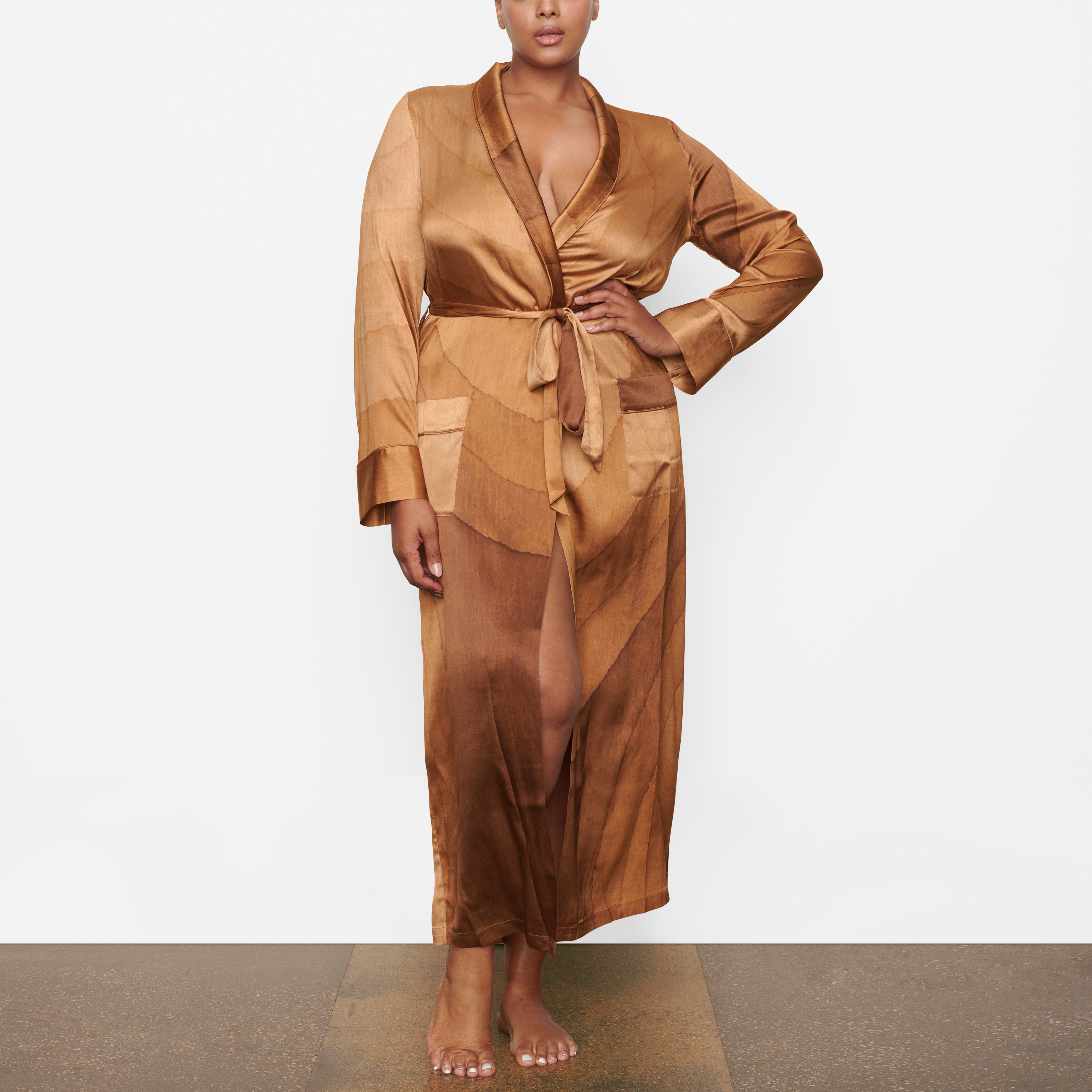 A MODEL STANDS FACING FORWARD WEARING THE SKIMS SILK SLEEP ROBE IN OAK | SEE: 2X, 3X, 4X