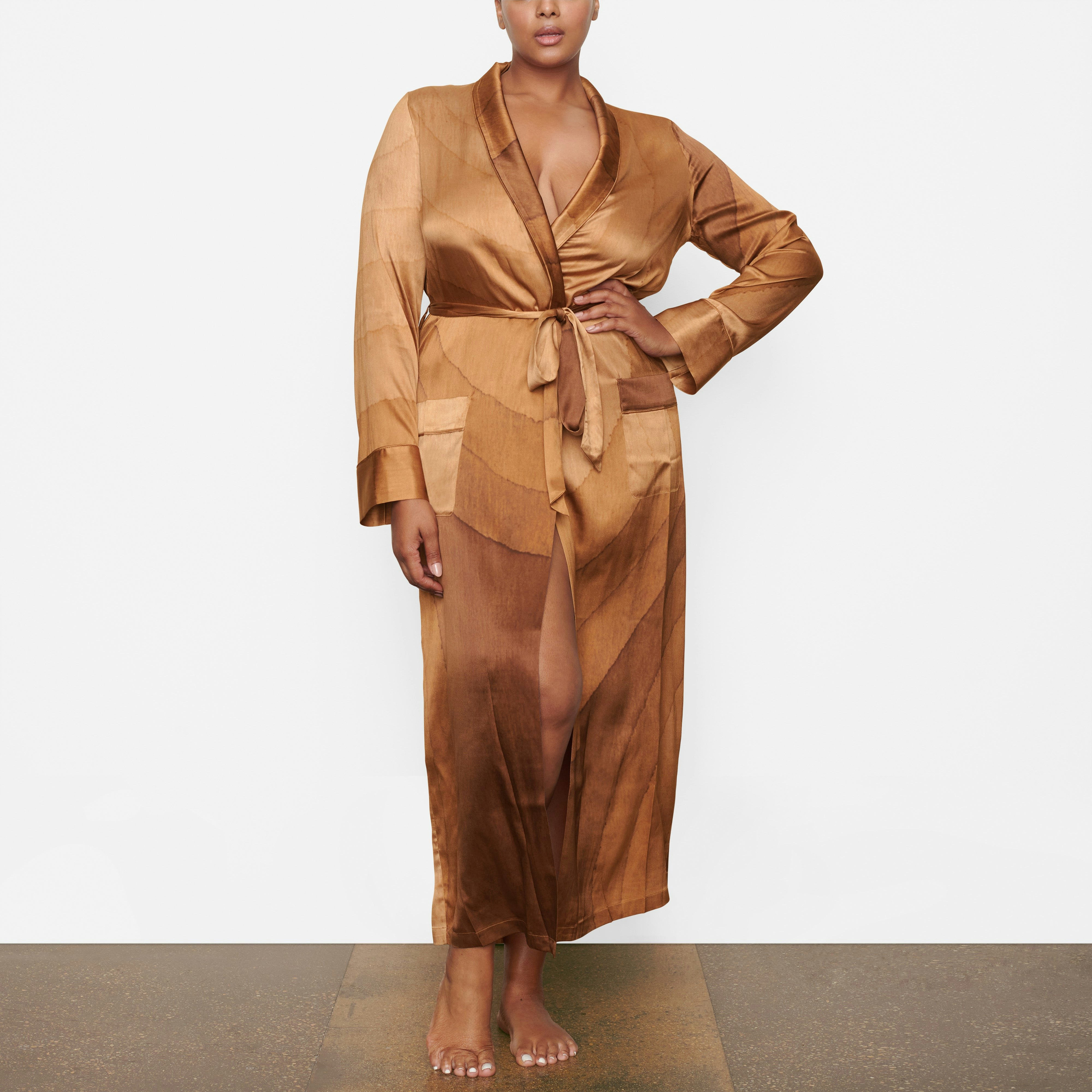 A MODEL STANDS FACING FORWARD WEARING THE SKIMS SILK SLEEP ROBE IN OAK | SEE: 2X, 3X, 4X