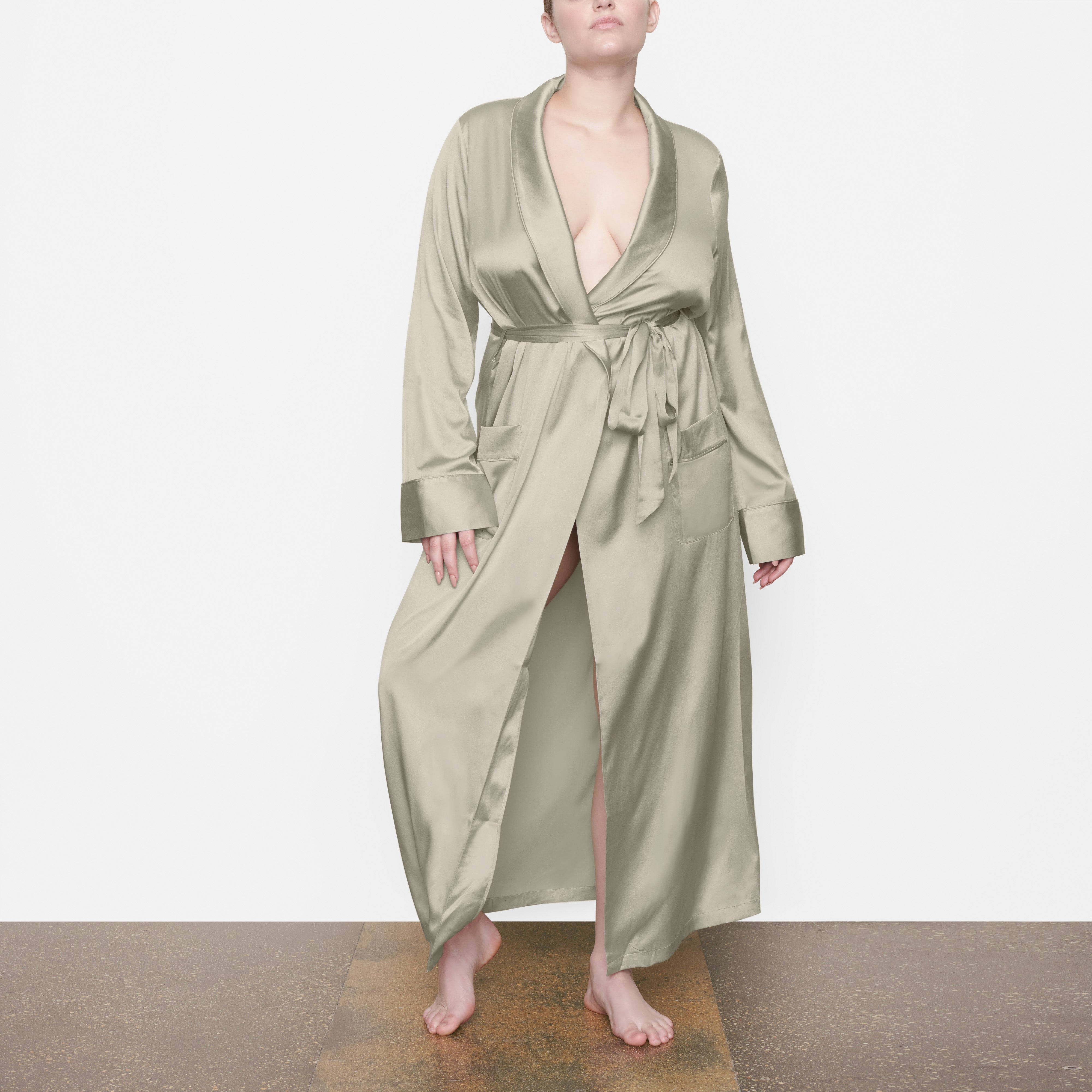 A MODEL STANDS FACING FORWARD WEARING THE SKIMS SILK SLEEP ROBE IN TALC | SEE: M, L, XL