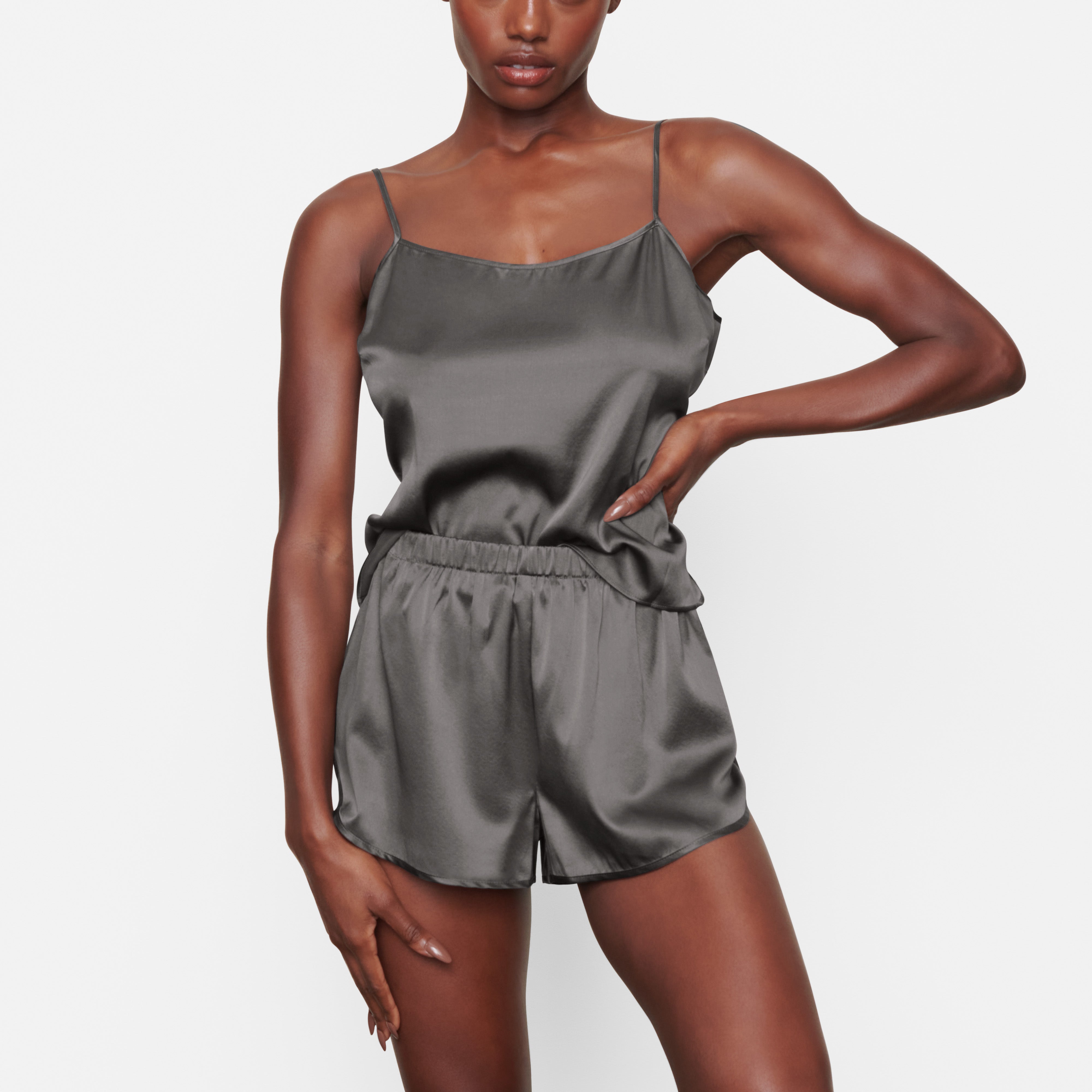 A MODEL STANDS FACING FORWARD WEARING THE SKIMS SILK SLEEP TAP SHORT IN GUNMETAL | SEE: XXS, XS, S