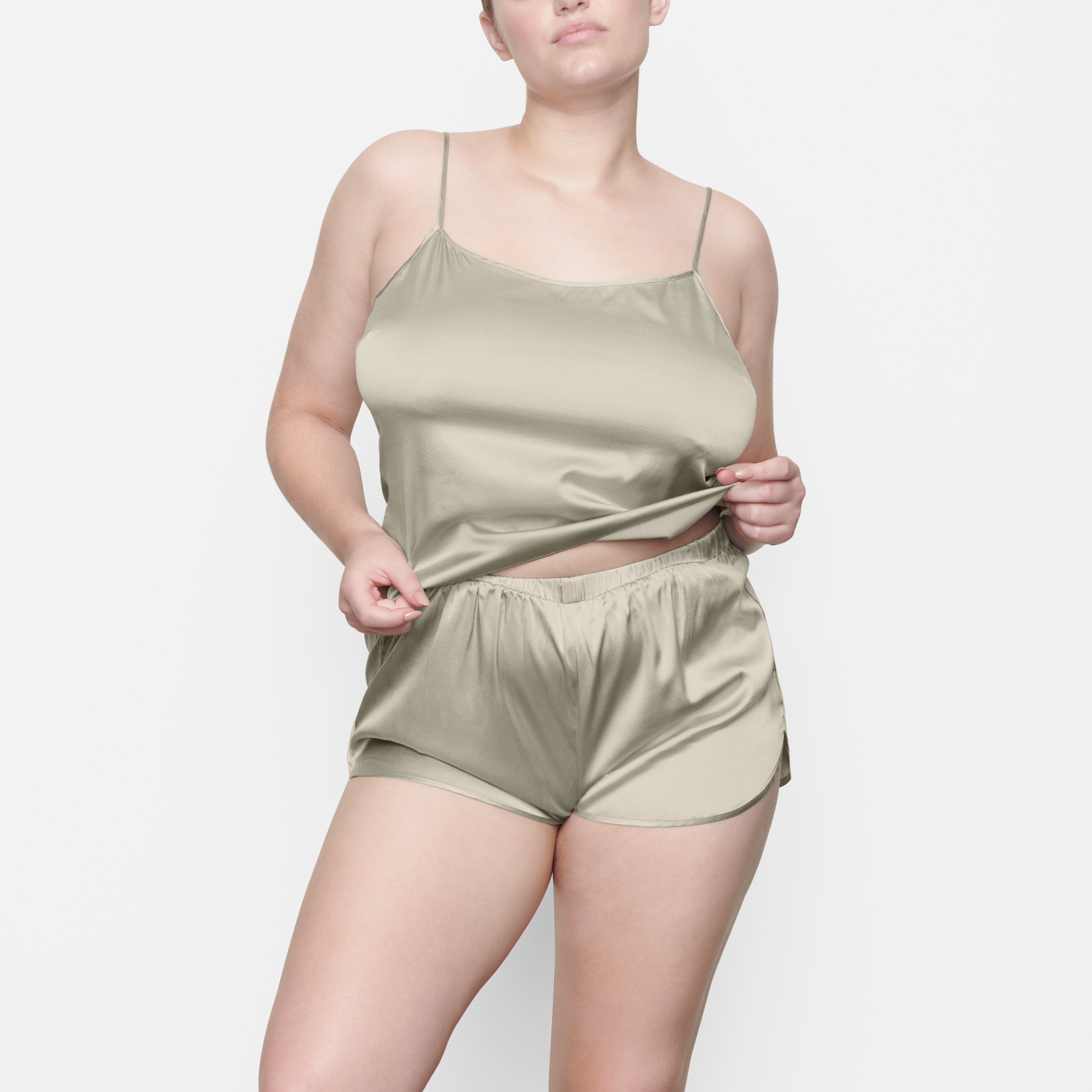 A MODEL STANDS FACING FORWARD WEARING THE SKIMS SILK SLEEP TAP SHORT IN TALC | SEE: M, L, XL