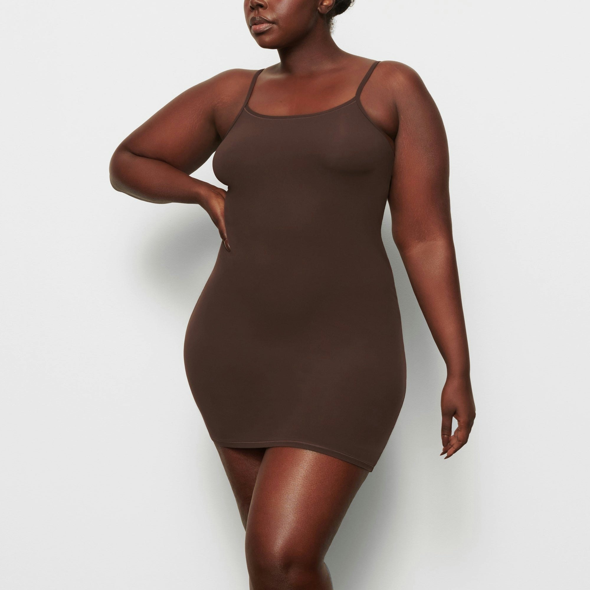 A MODEL STANDS FACING FORWARD WEARING THE SKIMS FITS EVERYBODY SLIP DRESS IN COCOA | SEE: 2X, 3X, 4X