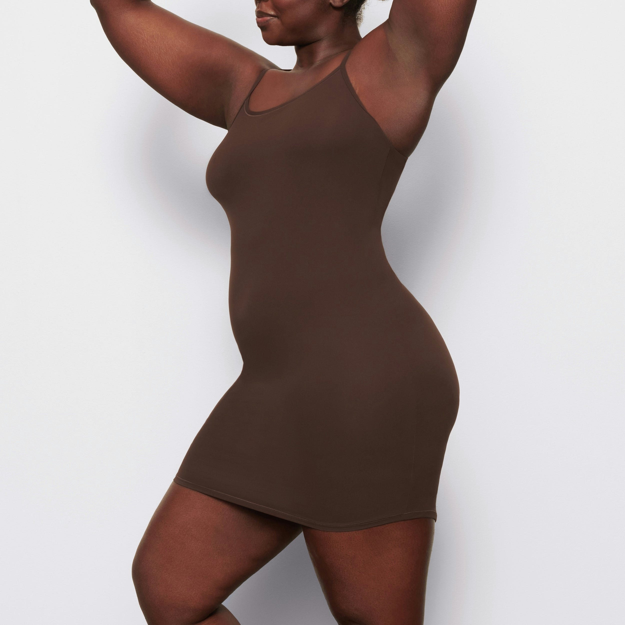 A MODEL STANDS SIDEWAYS SHOWING THE PROFILE OF THE FITS EVERYBODY SLIP DRESS | COCOA