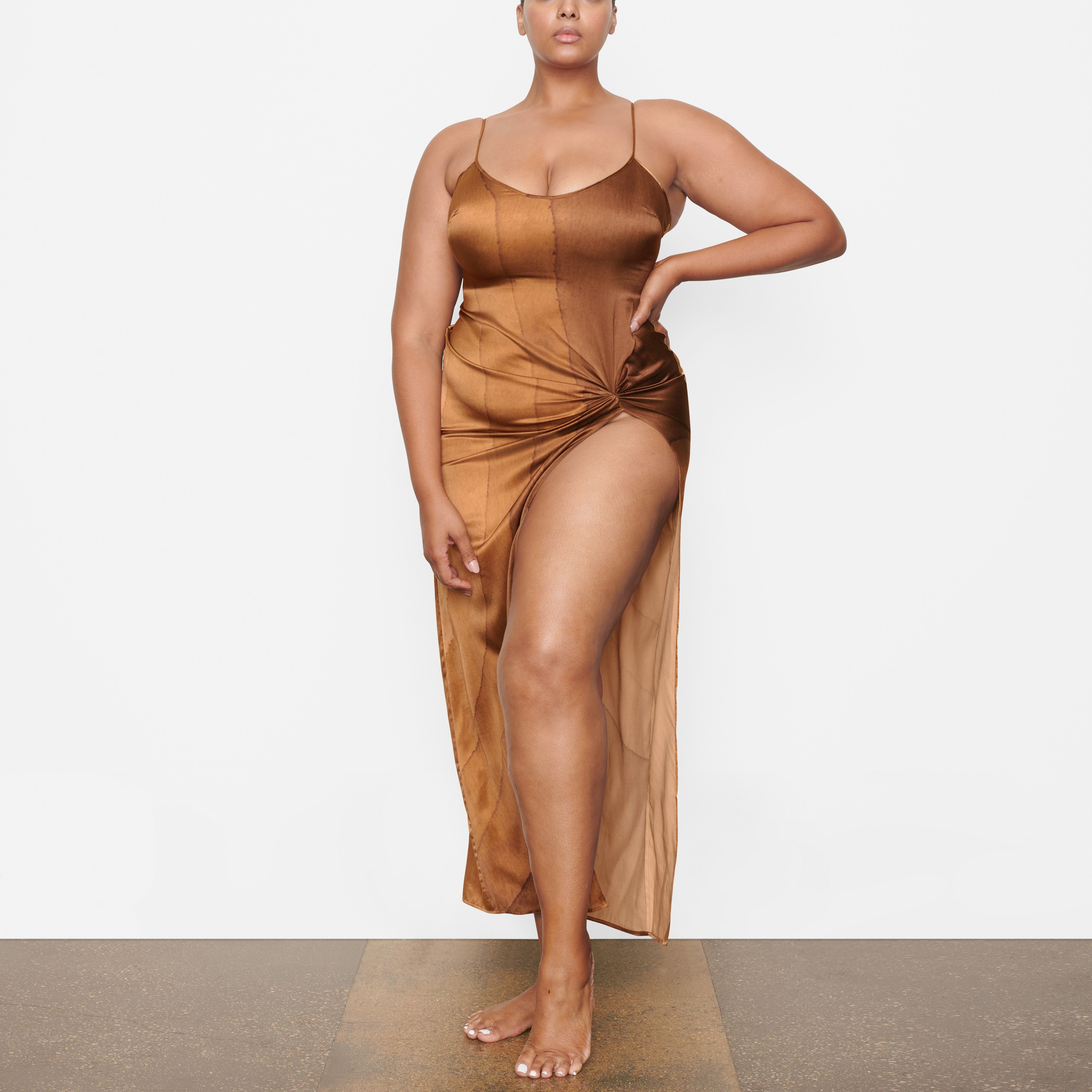 A MODEL STANDS FACING FORWARD WEARING THE SKIMS SILK SLEEP SLIP WITH HIGH SLIT IN OAK | SEE: 2X, 3X, 4X