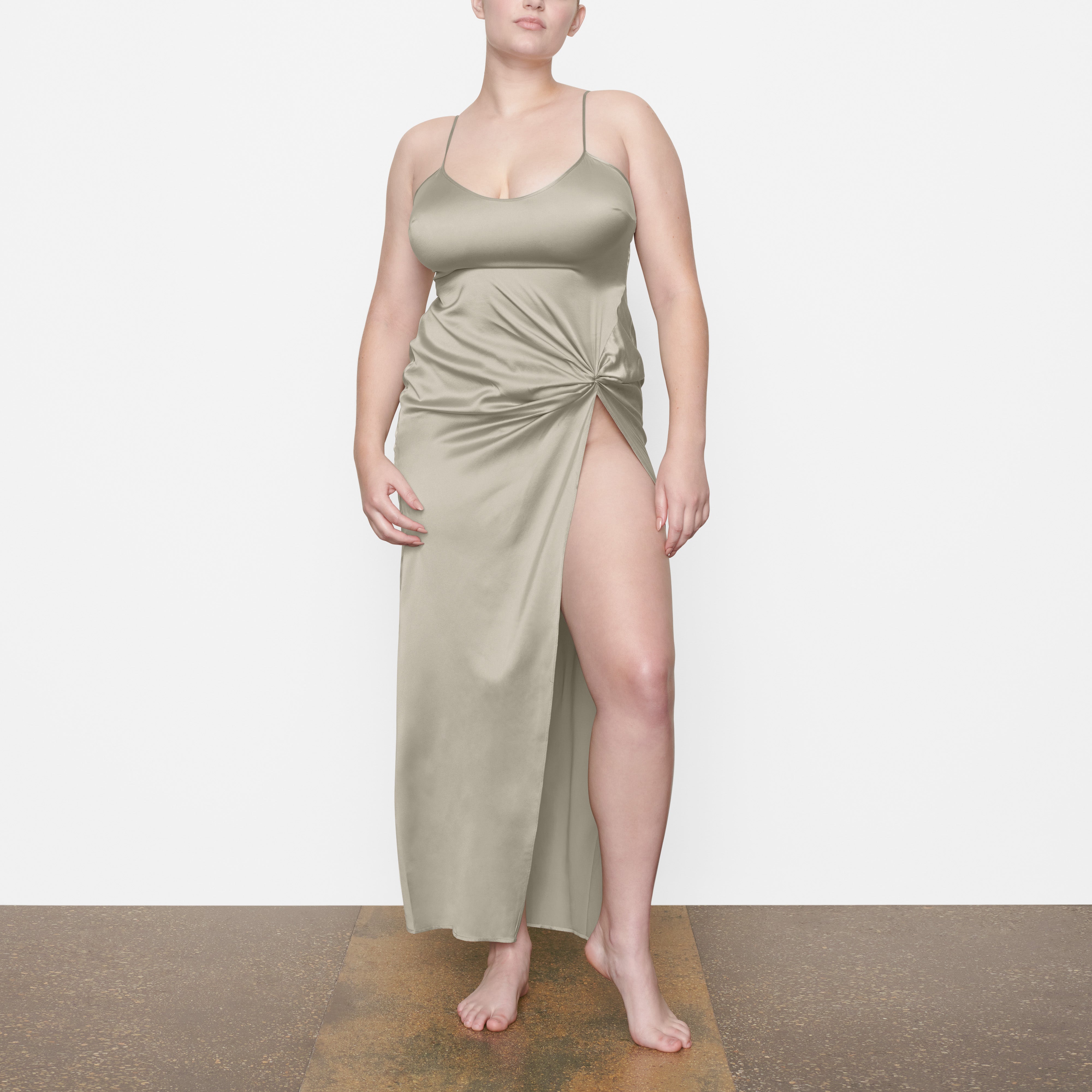 A MODEL STANDS FACING FORWARD WEARING THE SKIMS SILK SLEEP SLIP WITH HIGH SLIT IN TALC | SEE: M, L, XL