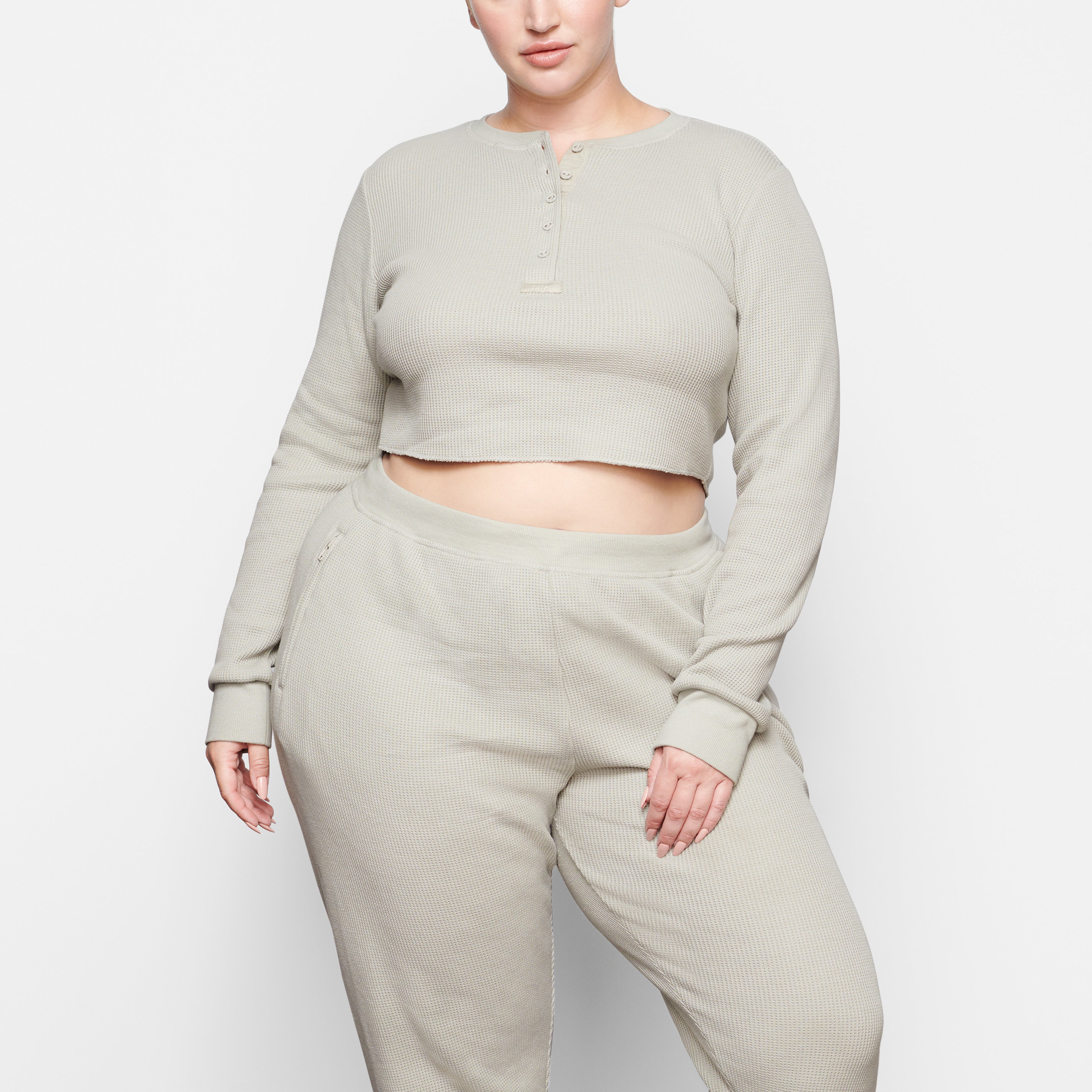 A MODEL STANDS FACING FORWARD WEARING THE SKIMS WAFFLE LONG SLEEVE CROP HENLEY IN TALC | SEE: 2X, 3X, 4X