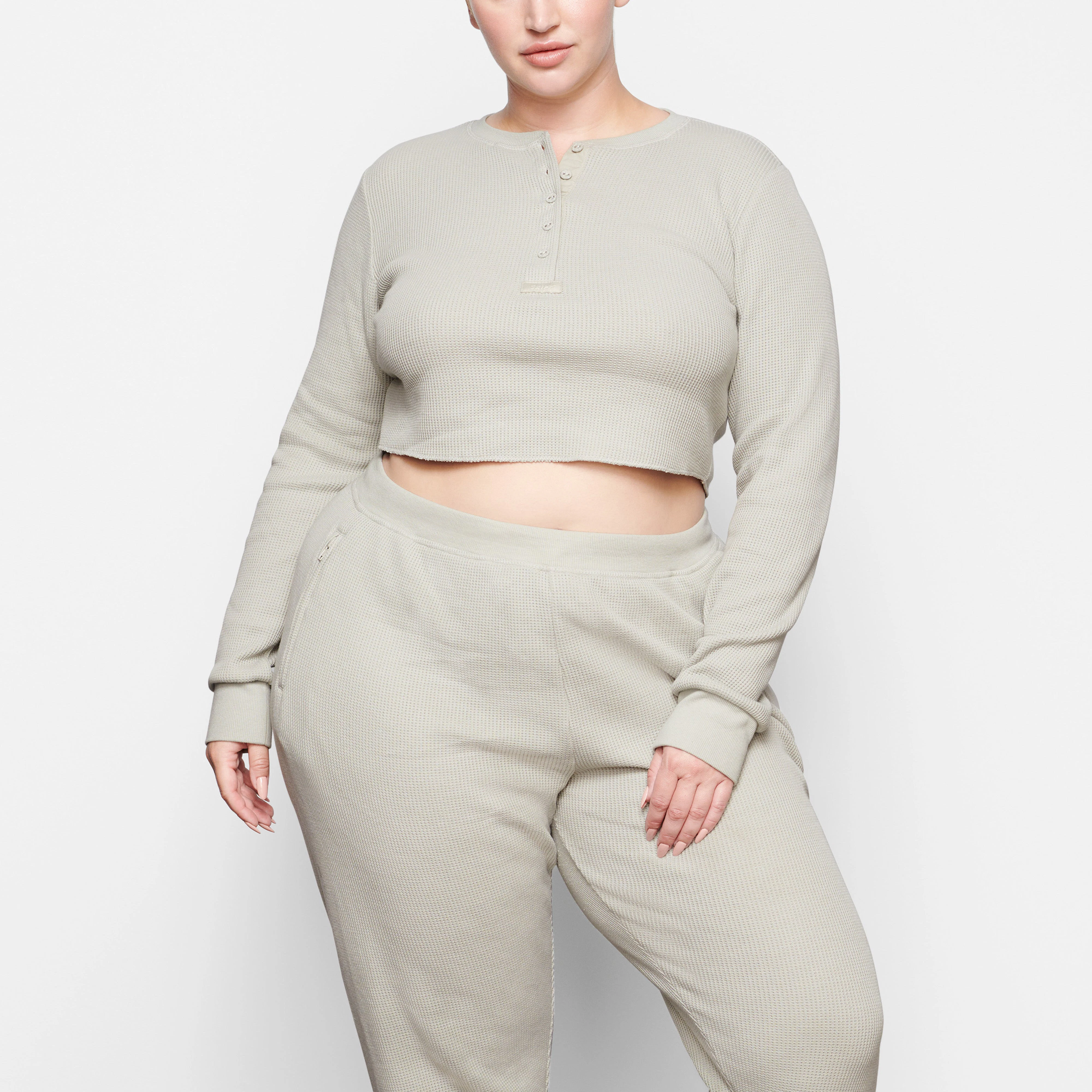 A MODEL STANDS FACING FORWARD WEARING THE SKIMS WAFFLE LONG SLEEVE CROP HENLEY IN TALC | SEE: 2X, 3X, 4X