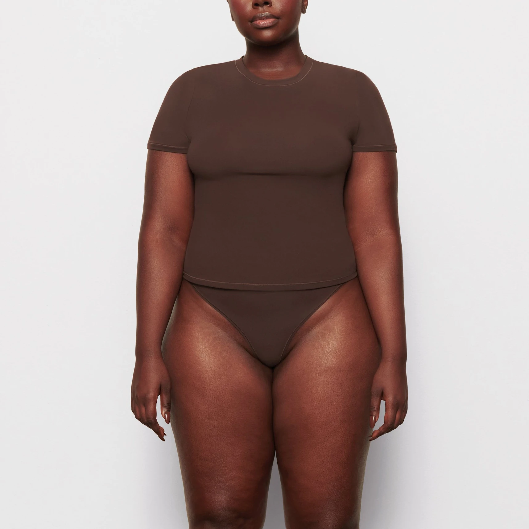 A MODEL STANDS FACING FORWARD WEARING THE SKIMS FITS EVERYBODY T-SHIRT IN COCOA