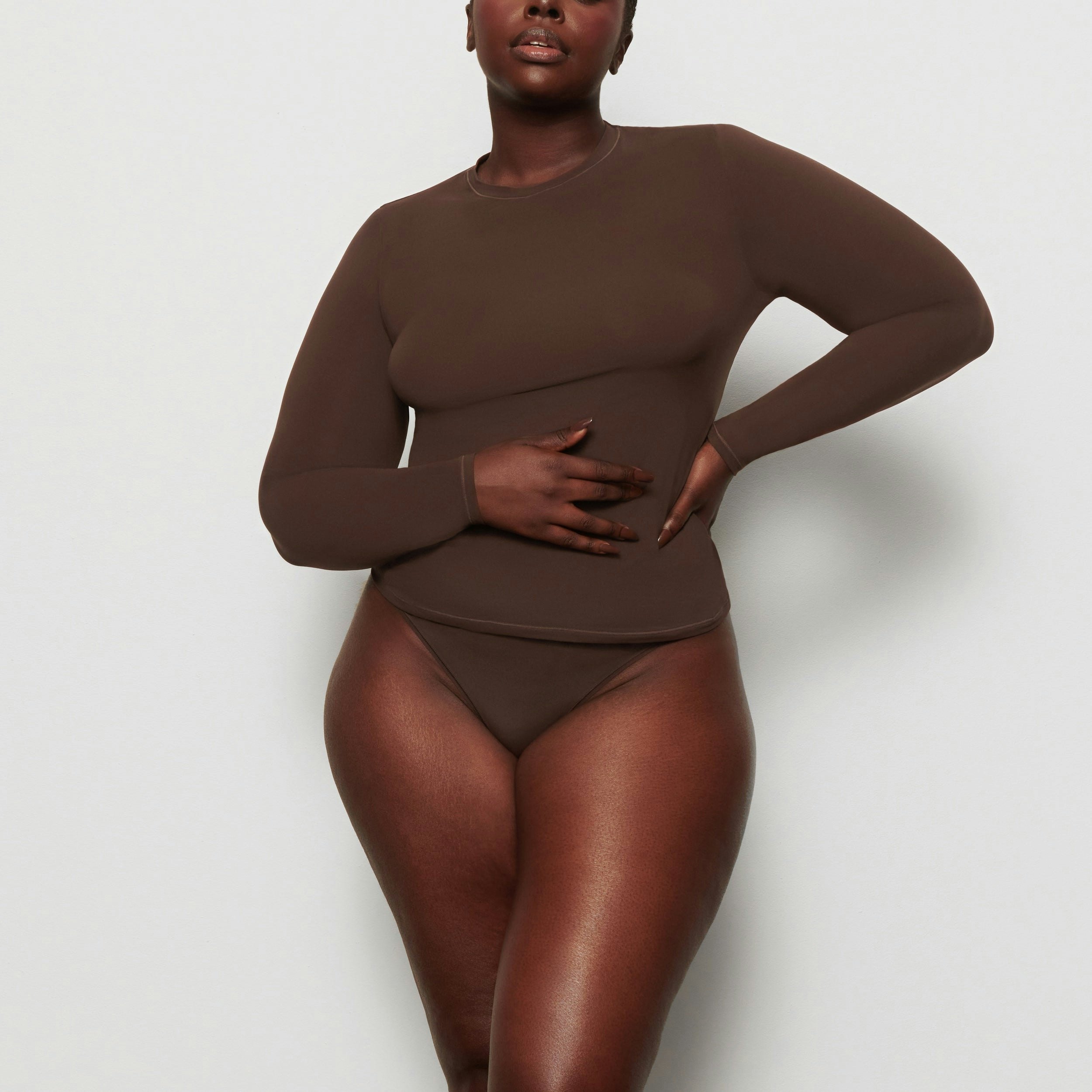 A MODEL STANDS FACING FORWARD WEARING THE SKIMS FITS EVERYBODY LONG SLEEVE T-SHIRT IN COCOA | SEE: 2X, 3X, 4X