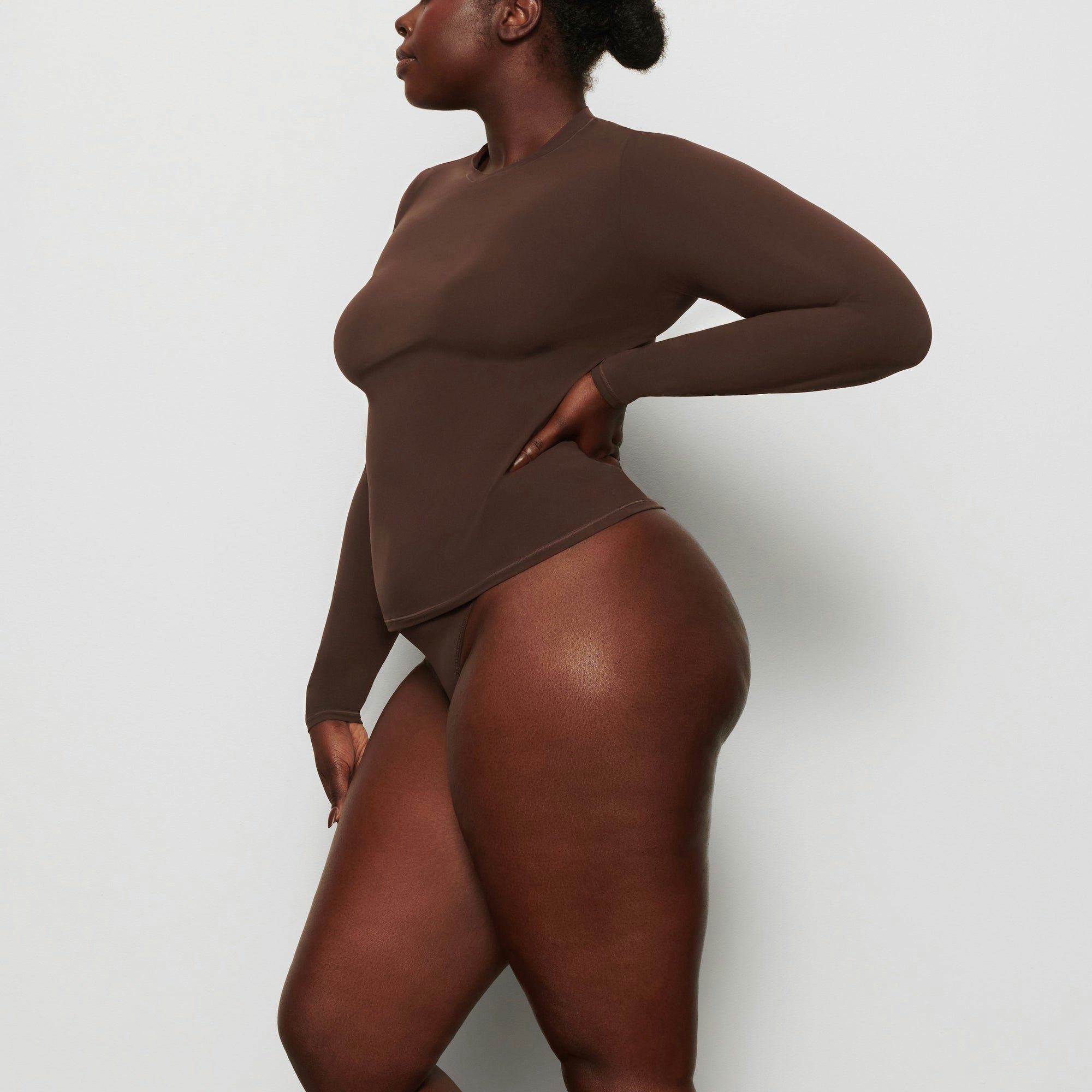 A MODEL STANDS SIDEWAYS SHOWING THE PROFILE OF THE FITS EVERYBODY LONG SLEEVE T-SHIRT | COCOA