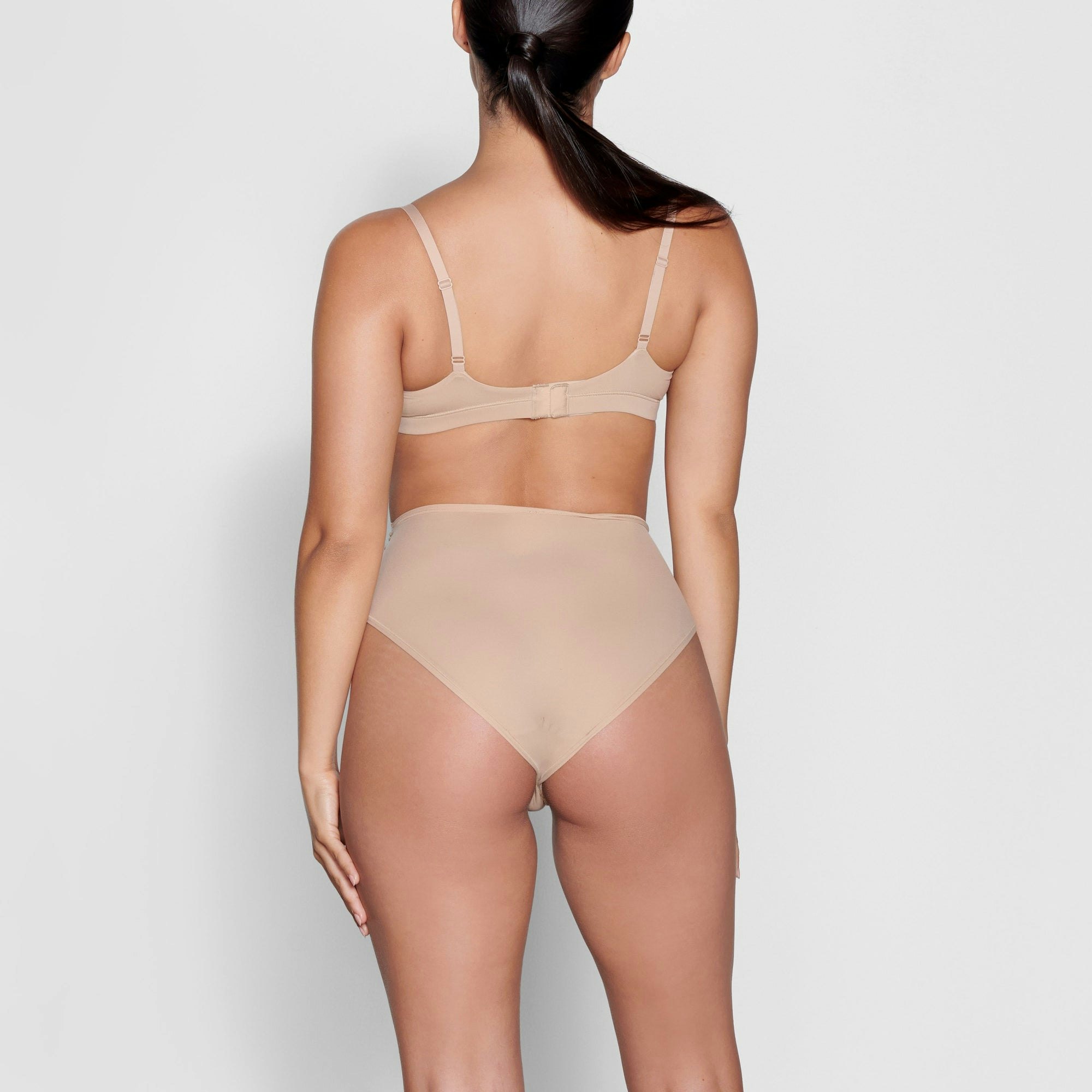 A MODEL STANDS WITH HER BACK TO THE CAMERA SHOWING THE FITS EVERYBODY FULL BRIEF | CLAY