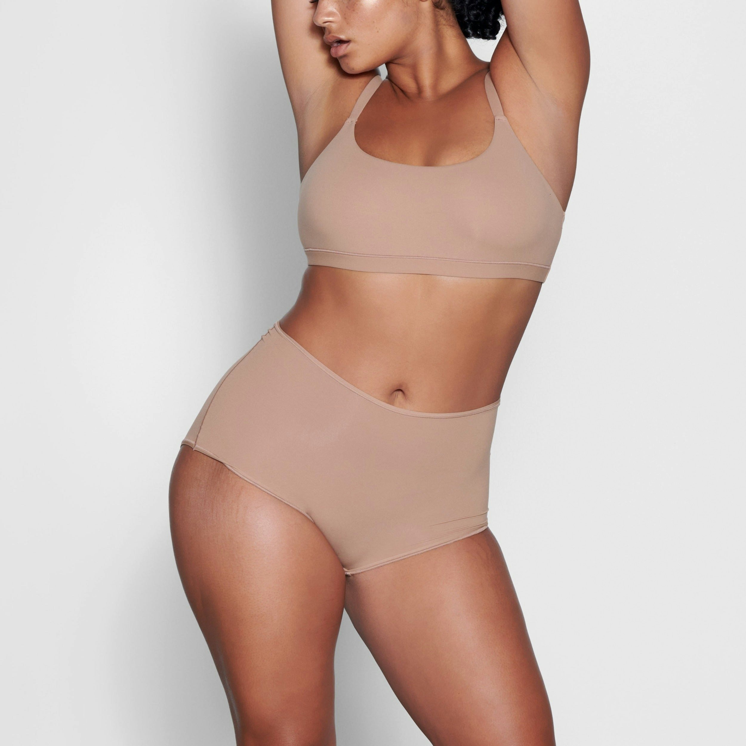 A MODEL STANDS FACING FORWARD WEARING THE SKIMS FITS EVERYBODY BOY SHORT IN SIENNA | SEE: M