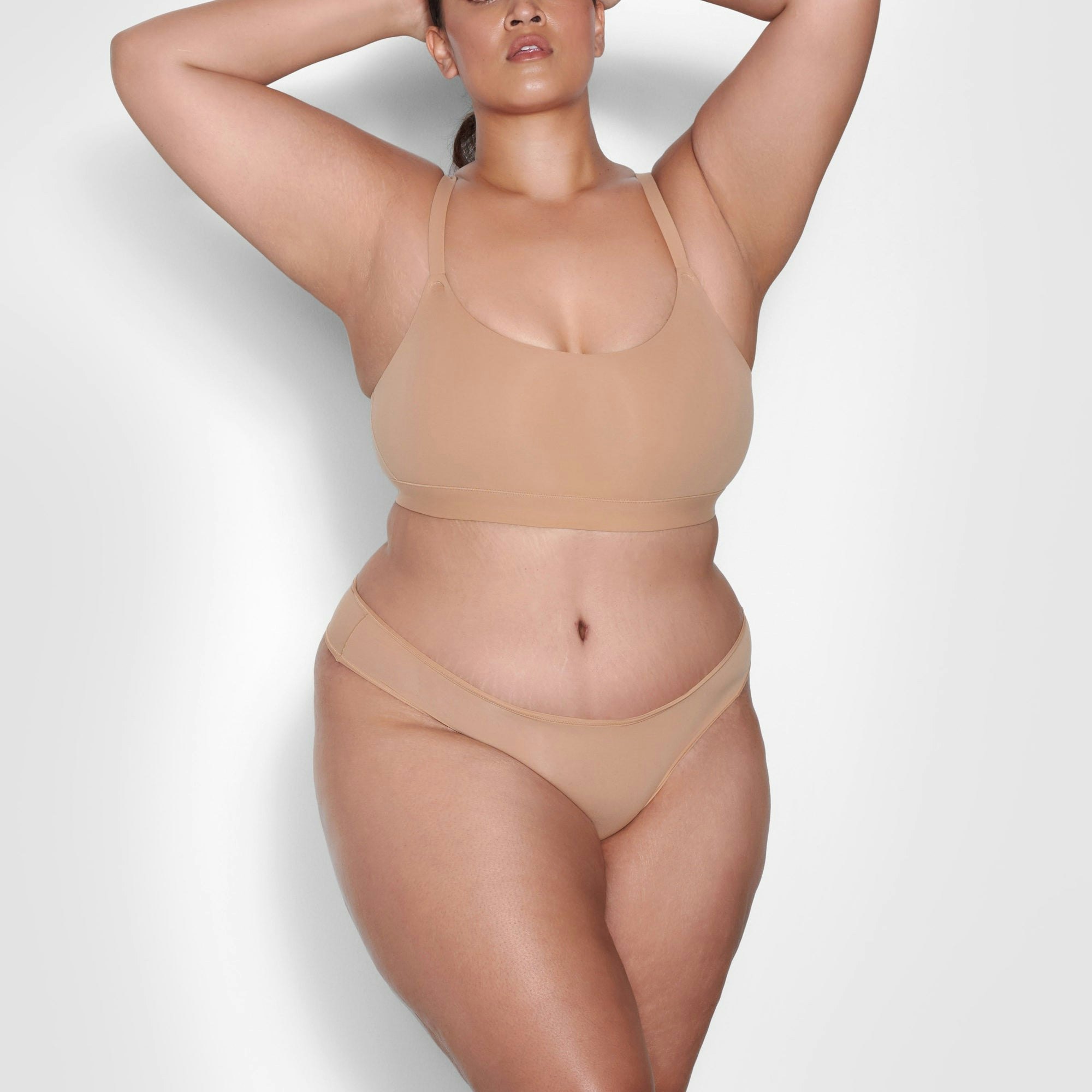 A MODEL STANDS FACING FORWARD WEARING THE SKIMS FITS EVERYBODY THONG IN OCHRE | SEE: 2X, 3X, 4X