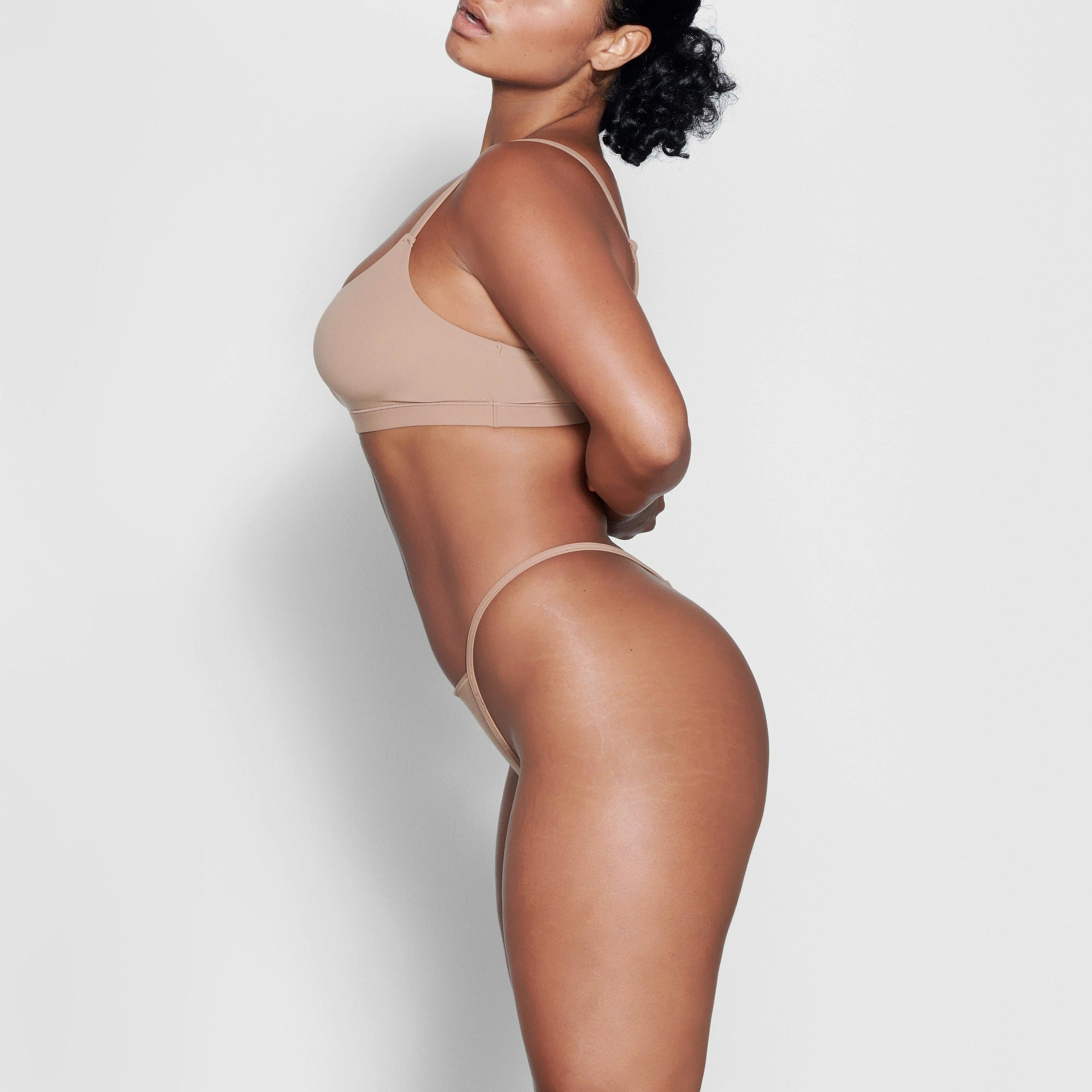 A MODEL STANDS SIDEWAYS SHOWING THE PROFILE OF THE FITS EVERYBODY T STRING THONG | SIENNA