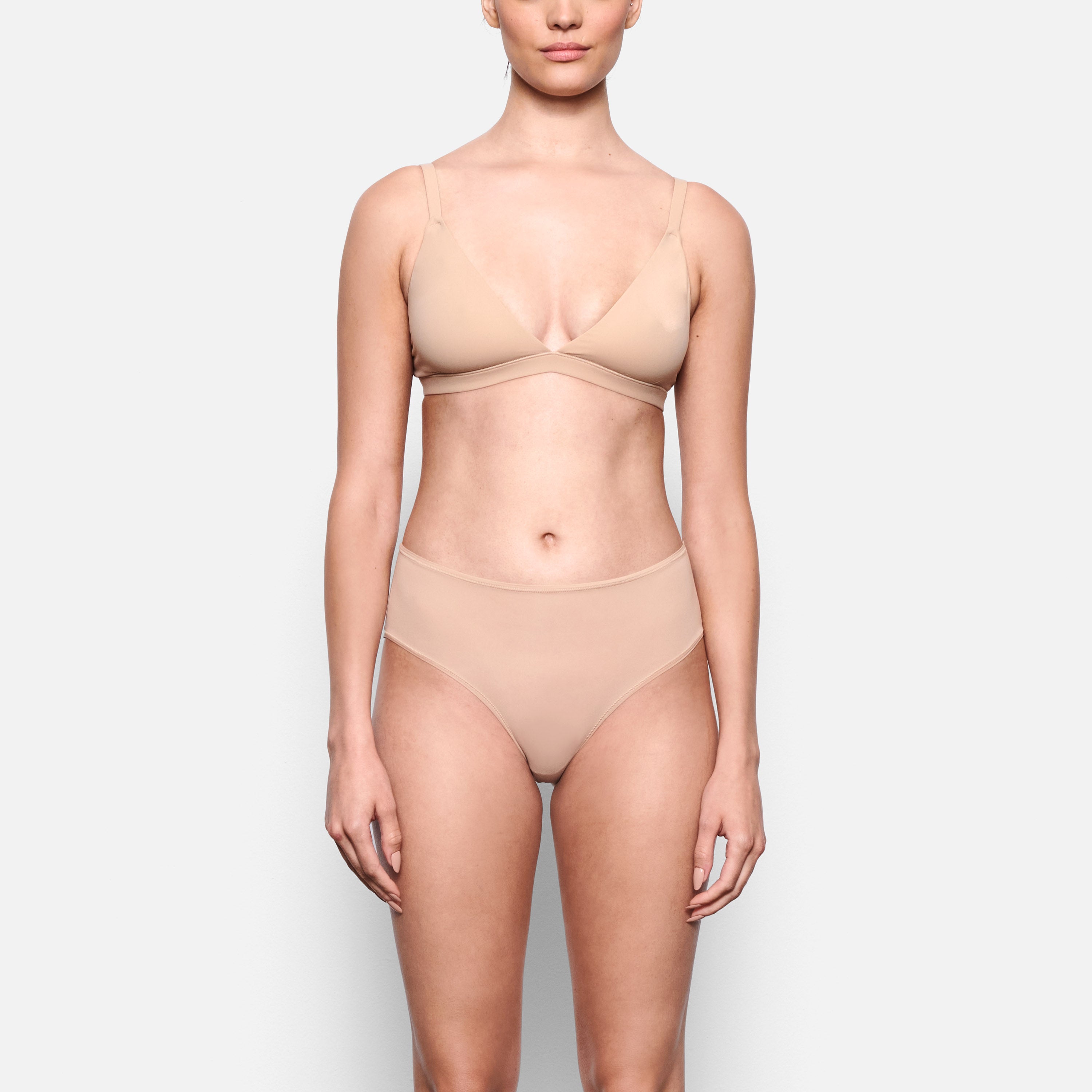 A MODEL STANDS FACING FORWARD WEARING THE SKIMS FITS EVERYBODY MID RISE BRIEF IN CLAY | SEE: XXS, XS, S