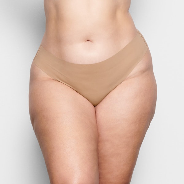 A MODEL STANDS FACING FORWARD WEARING THE SKIMS FREE CUT MID WAIST THONG IN CLAY | SEE: 2X, 3X, 4X | FOCUS: 0.1, 0.9, 0.9