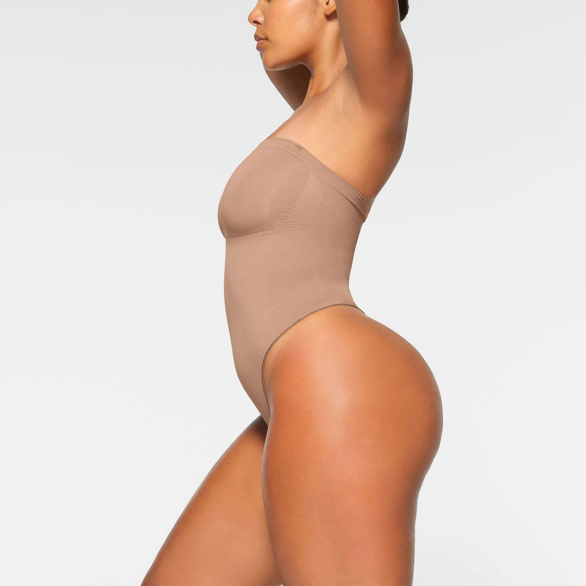 SEAMLESS SCULPT STRAPLESS THONG BODYSUIT WORN BY A MODEL IN SIDE VIEW