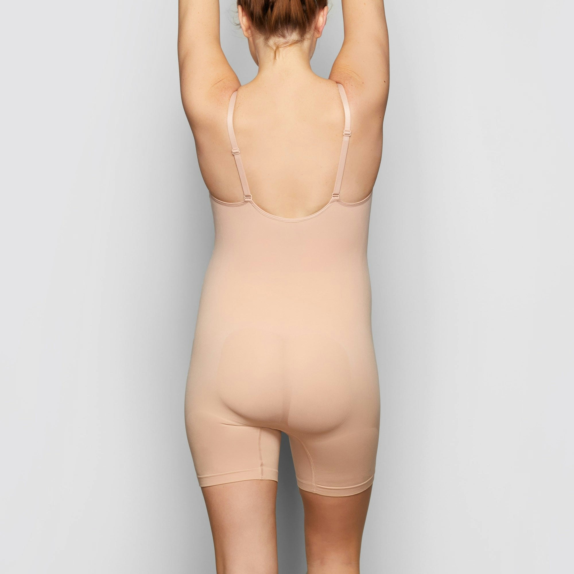 A MODEL STANDS SIDEWAYS SHOWING THE PROFILE OF THE MATERNITY SCULPTING BODYSUIT MID THIGH | MICA
