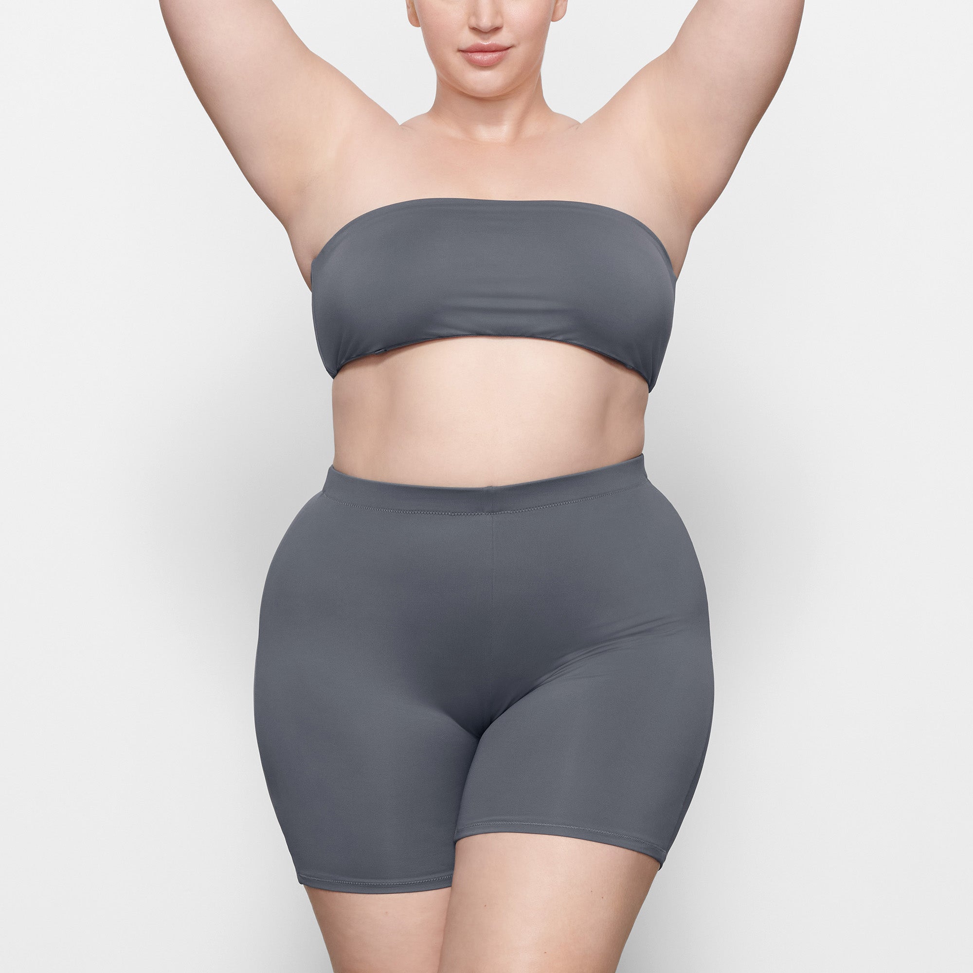 A MODEL STANDS FACING FORWARD WEARING THE SKIMS SWIM MID WAIST SHORT IN GUNMETAL | SEE: 2X, 3X, 4X