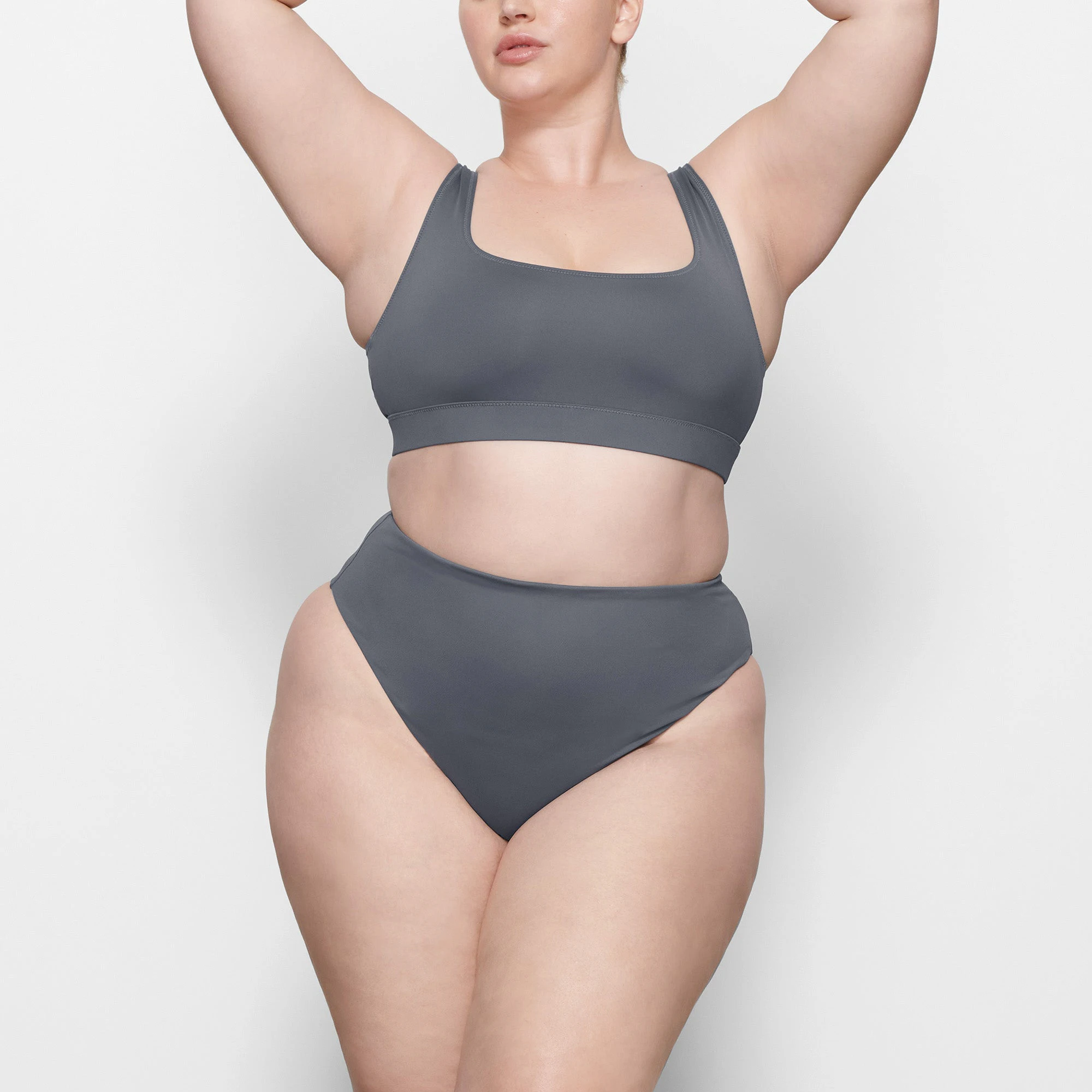 A MODEL STANDS FACING FORWARD WEARING THE SKIMS SWIM TANK BIKINI TOP IN GUNMETAL | SEE: 2X, 3X, 4X