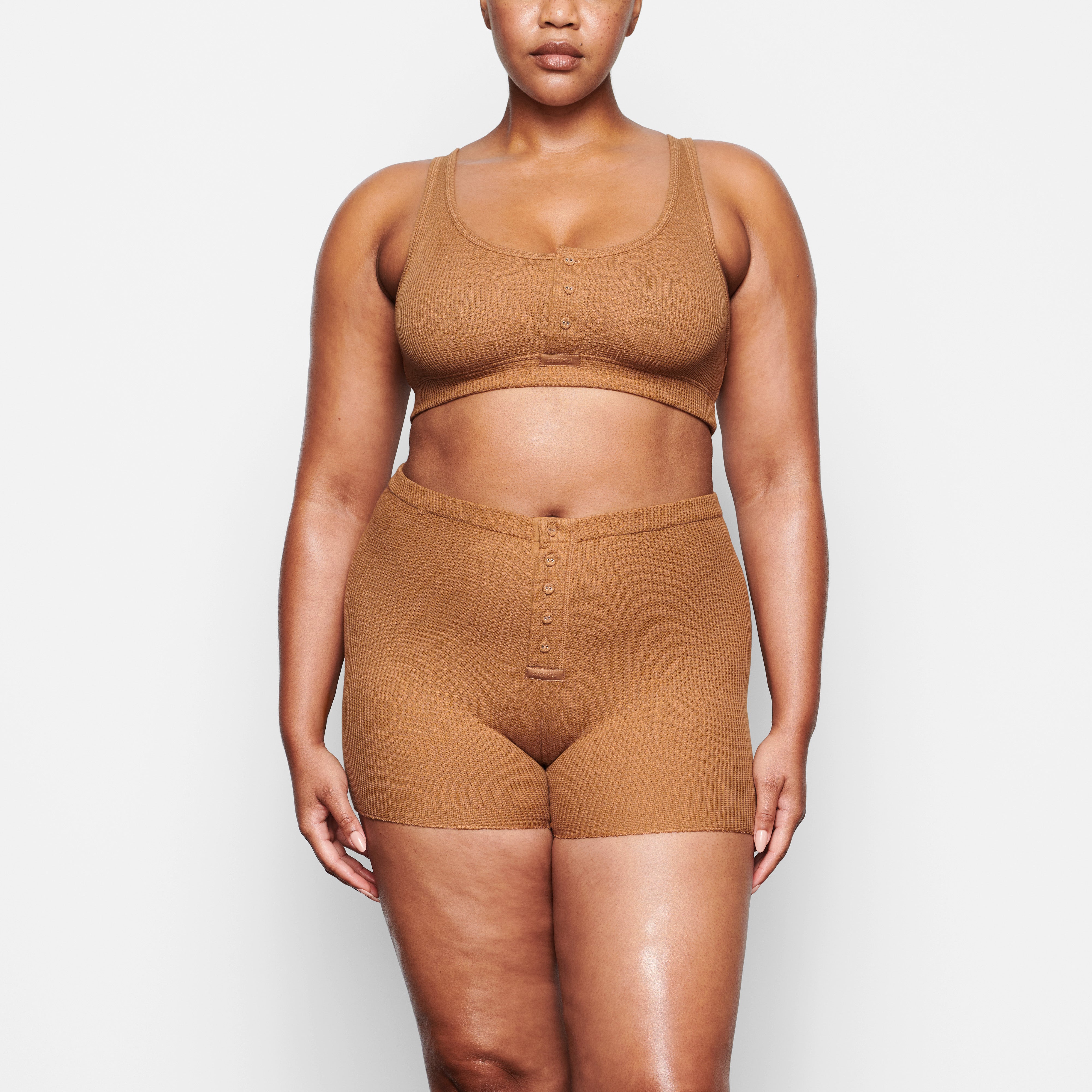 A MODEL STANDS FACING FORWARD WEARING THE SKIMS WAFFLE SHORT IN CAMEL | SEE: M, L, XL